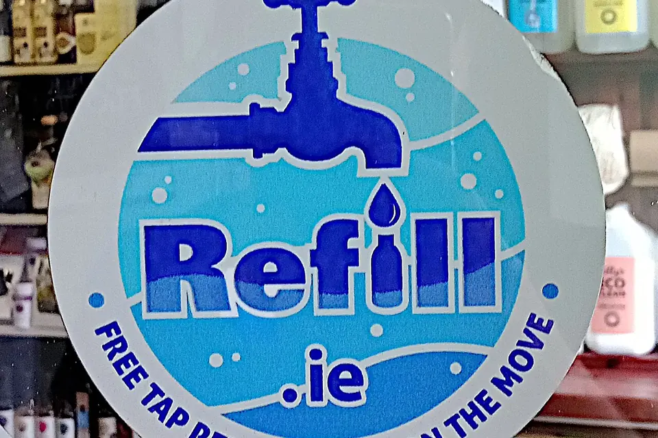 Autocollant rond bleu signalant un point de remplissage gratuit de gourdes, collé sur la porte d'une épicerie