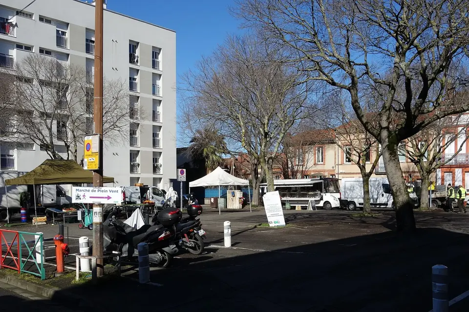 Place de quartier à Toulouse en fin de matinée de marché, avec quelques étals et barnums encore installés devant des immeubles