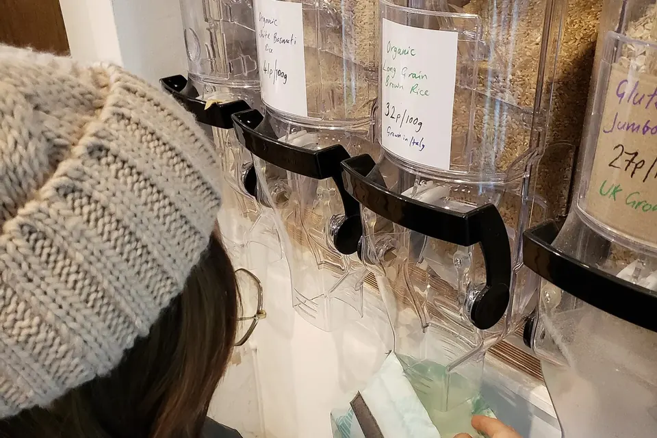 Une personne remplit son propre sac de riz complet à un distributeur à gravité dans une épicerie sans emballage
