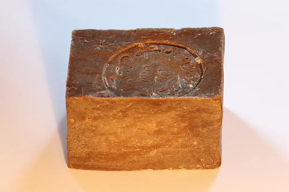 Pain de savon d'Alep brun-vert, de forme cubique, posé sur un fond blanc
