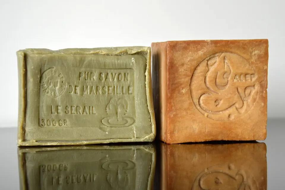 Deux pains de savon posés côte à côte, l'un vert olive estampillé savon de Marseille, l'autre brun orangé estampillé